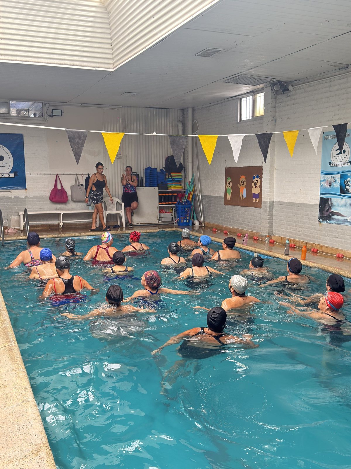 Profesoras guiando la clase de aquagym desde el borde de la pileta